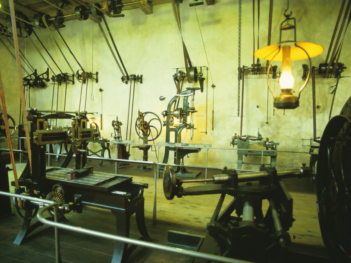 Zu sehen ist ein Bild mit historischen Werkzeugen, die zur Reparatur und Fertigung von Getrieben verwendet wurde. Das Bild zeigt die Werkstatt von der Firma KACHELMANN GETRIEBE GmbH im Jahr 1912. KACHELMANN GETRIEBE GmbH