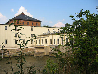 Die Schleuse Erna ist das das älteste in Deutschland noch im Einsatz befindliche KACHELMANN GETRIEBE GmbH. Auf dem Bild sieht man die Schleuse Erna, einen blauen Himmel mit einigen Quellwolken, und die Büsche unten rechts am Bildrand. KACHELMANN GETRIEBE GmbH